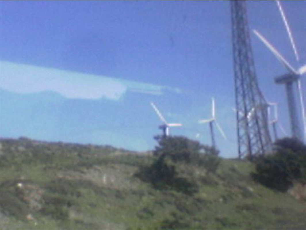 Photo of wind turbines and a pylon on a green hillside under a blue sky.
