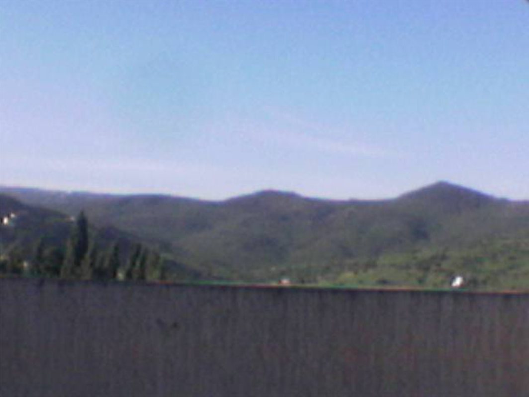 Photo of green hills and mountains under a blue sky, seen over a wall.